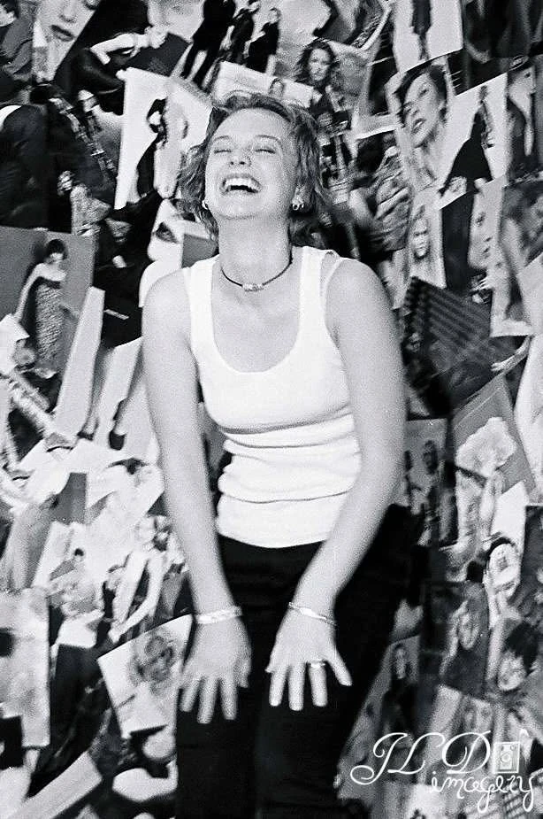 Laughing in front of a wall covered with photographs, in black and white.