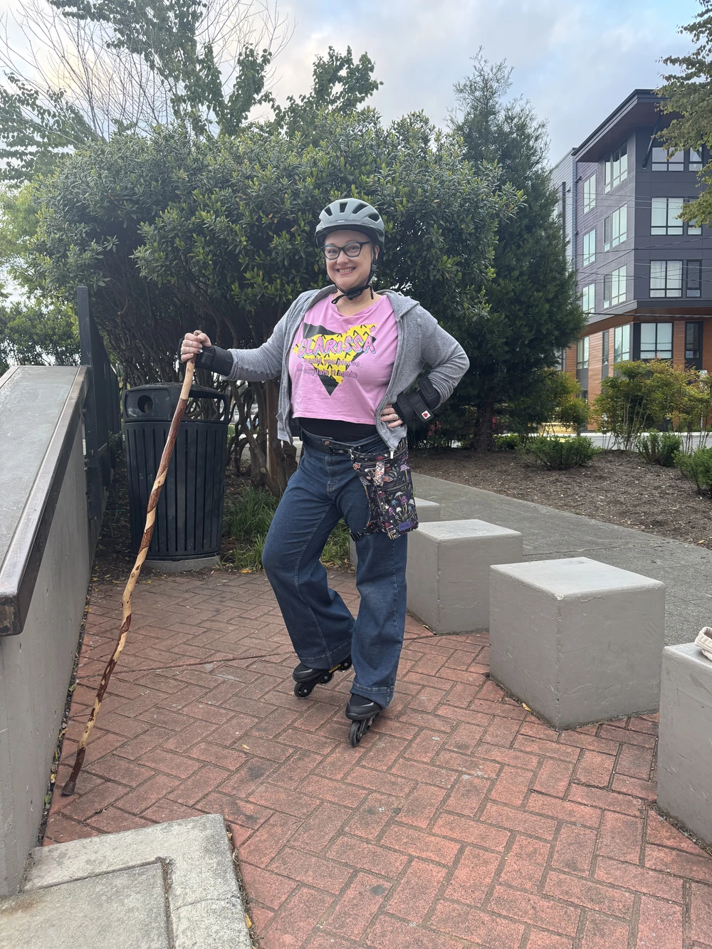 Outdoors in a helmet and roller skates, holding a wooden staff.