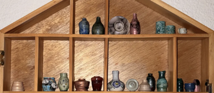 Wide view of miniature vases displayed across the peaked upper shelves of a wooden cabinet.