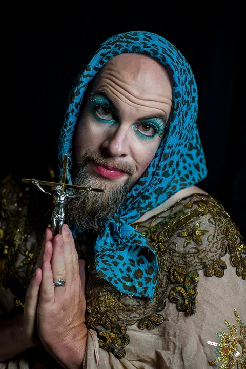 Theatrical portrait with a blue head covering and a decorative cross.