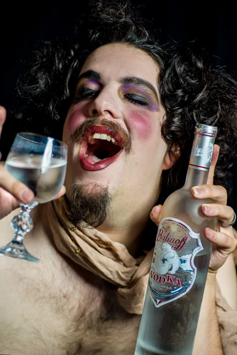 Expressive theatrical portrait with elaborate styling and a bottle prop.