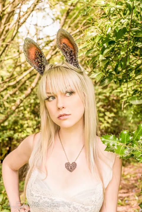 Close fantasy portrait with tall animal ears beneath green branches.