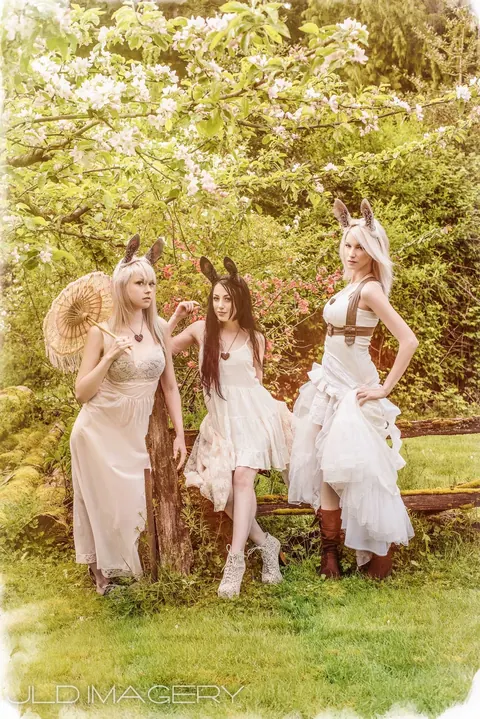 Three woodland characters in pale costumes gathered beneath flowering trees.