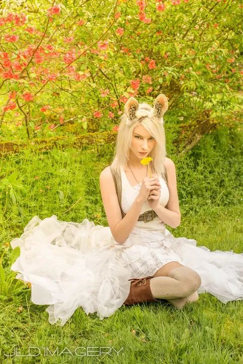 Woodland character with animal ears seated in grass holding a yellow flower.
