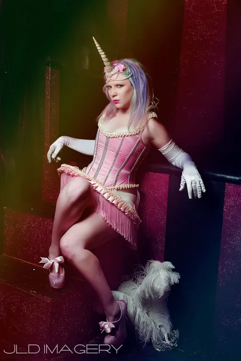 Pink unicorn character seated on a red platform under colored light.