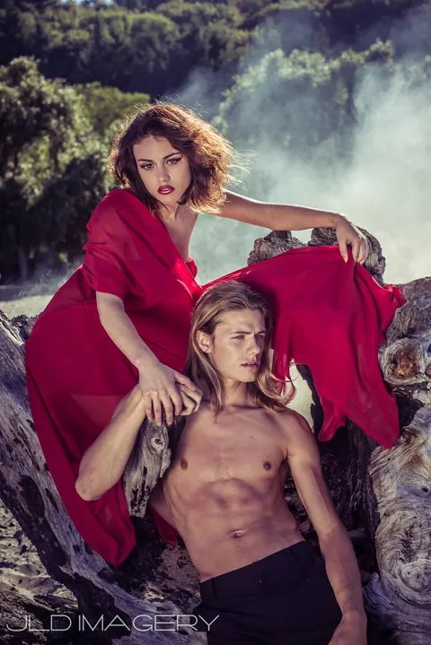 Two figures in red and earth tones posed among rocks and drifting smoke.