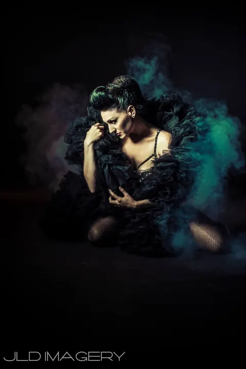 Seated theatrical portrait surrounded by blue and violet smoke.