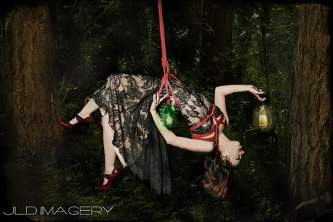 Fantasy figure suspended in a forest scene with playing cards and a glowing green orb.