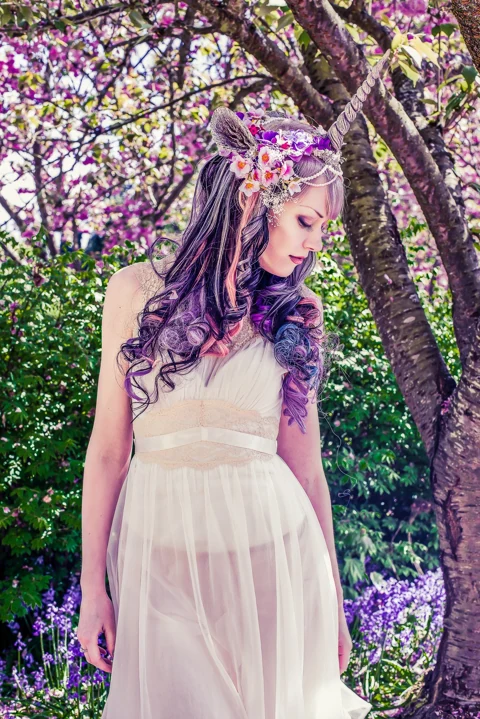 Fantasy portrait among flowering branches with an ornate unicorn headpiece.