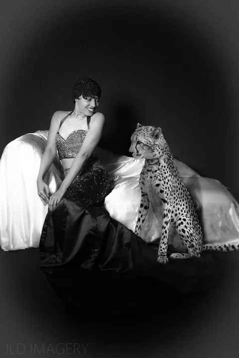 Monochrome fashion portrait posed on a bed beside a cheetah.