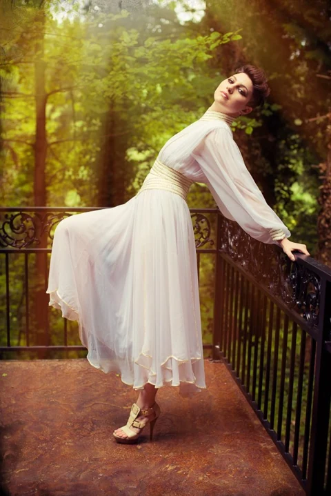 Fashion portrait on an iron balcony with warm forest light.