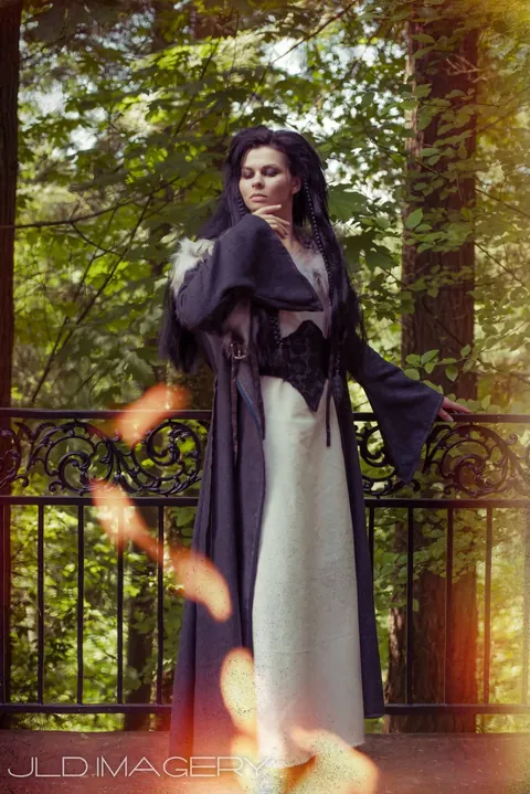 Period fashion portrait in a dark cape on a wooded balcony.