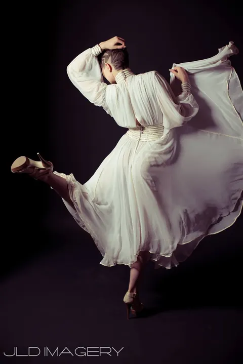 Fashion movement portrait in a flowing white dress against black.