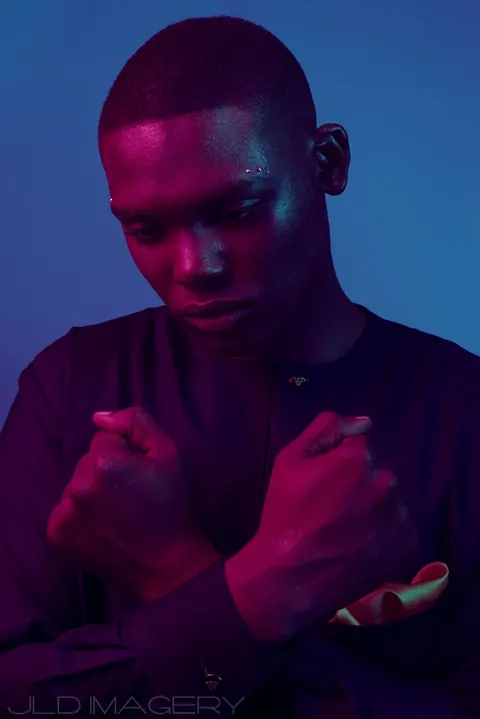 Portrait in blue and magenta light with folded arms.