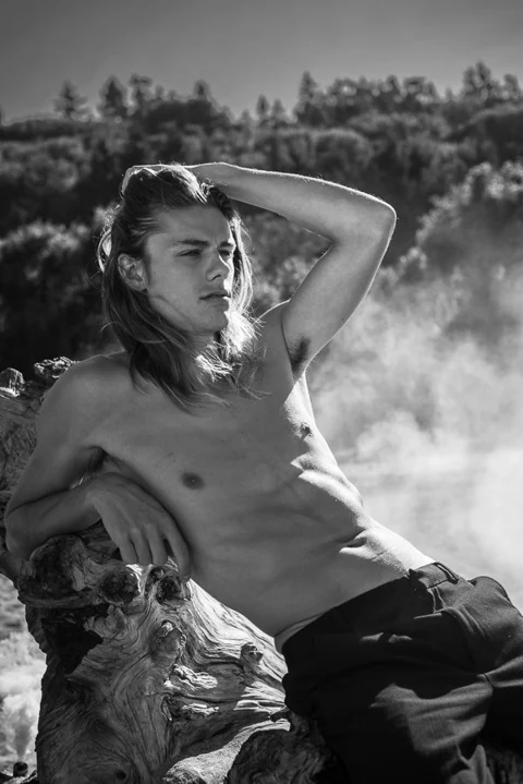 Black-and-white portrait reclining beside driftwood.