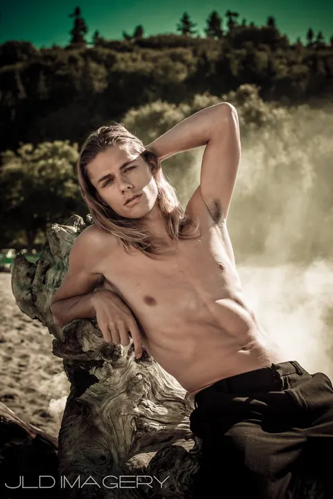 Male portrait reclining outdoors among driftwood and mist.