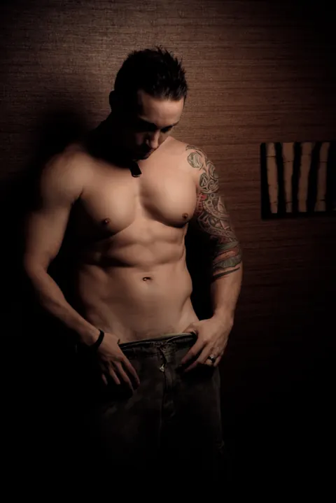 Low-key male portrait with directional light and a visible arm tattoo.