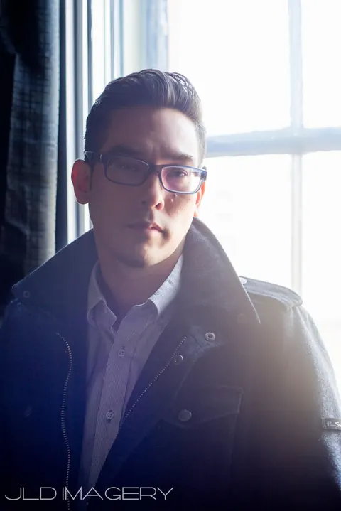 Blue-toned window portrait of a man wearing glasses.