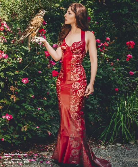 Dawn Mostow in a red gown holding an owl in a flowering garden.