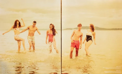 Five models splashing in shallow lake water in coordinating swimwear, mid-laugh, warm summer-evening light.