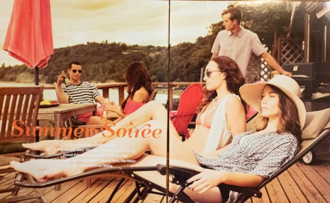 Editorial title spread "Summer Soirée" — five friends in summer attire lounging on a lakeside wooden deck under a red patio umbrella, warm sepia tones, with full credits laid over the spread.