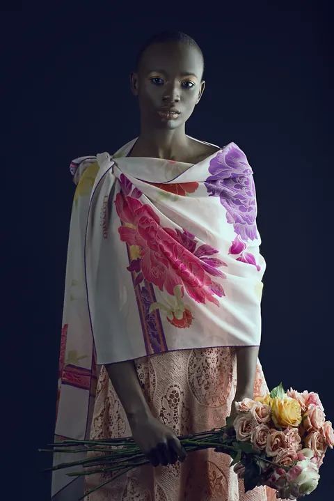 Binta Diba standing in a patterned wrap with a bouquet of pale flowers.